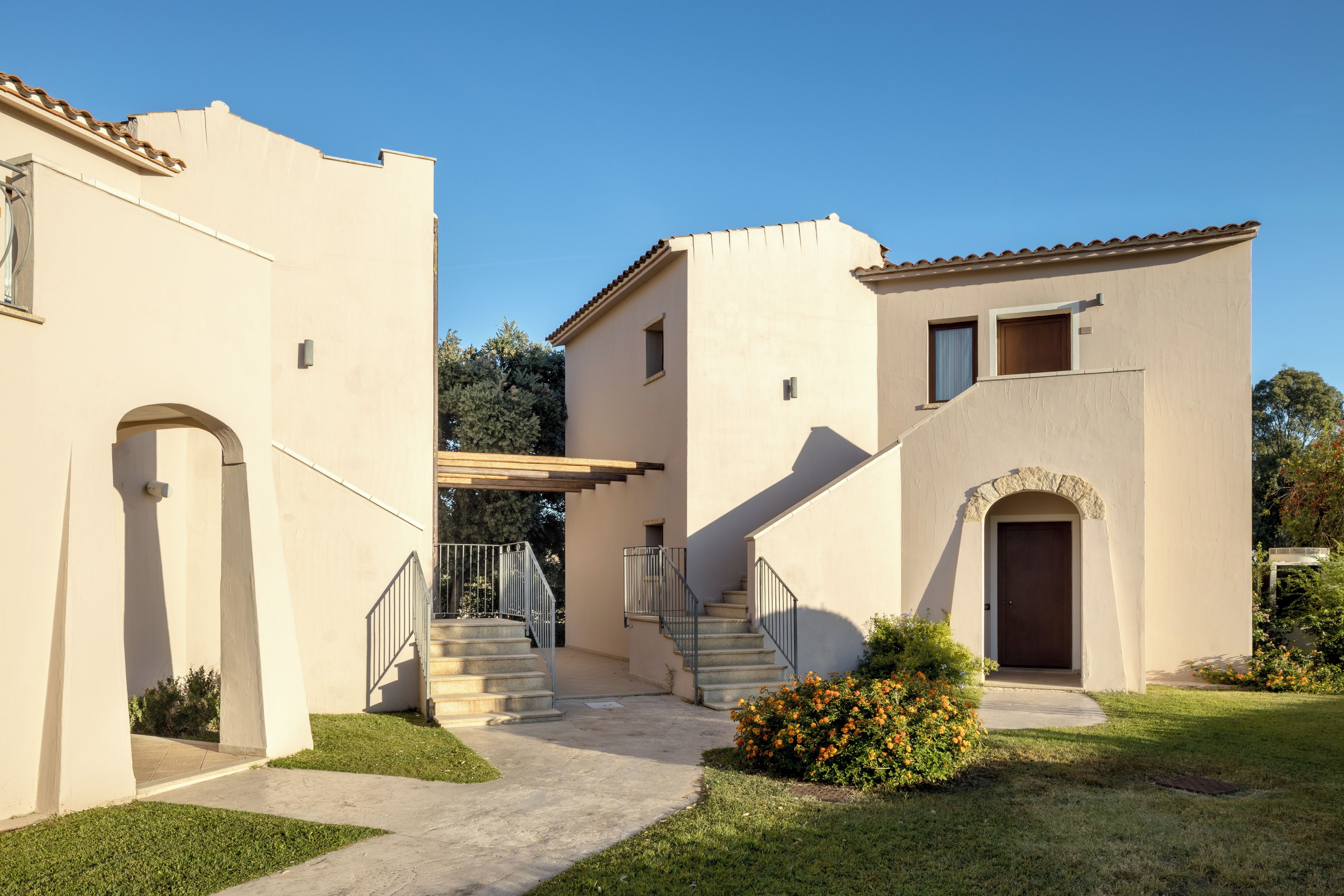 A building with a staircase leading to a door, a small garden with flowers, and a clear blue sky.