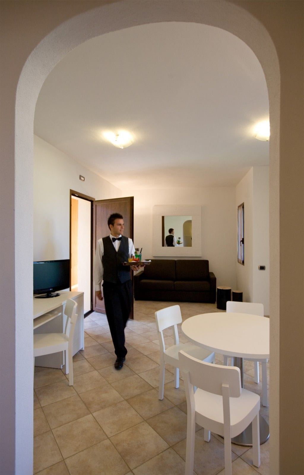 A hotel room with a dining area, a TV, a sofa, and a mirror.
