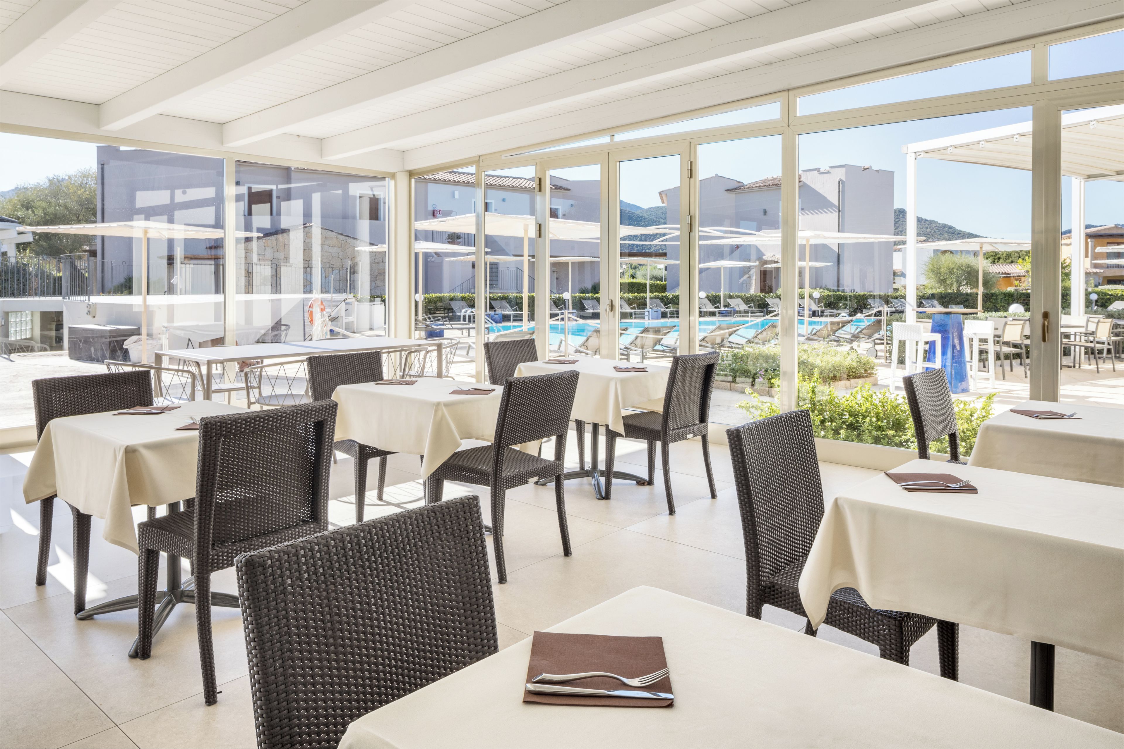 An outdoor dining area with tables and chairs, overlooking a pool and buildings.