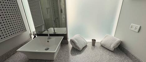 A bathroom with a white sink, two towels, a cup, and a glass shower enclosure.