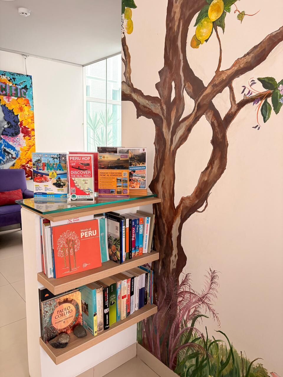 Une bibliothèque remplie de livres de voyage et une fresque représentant un arbre aux fruits.