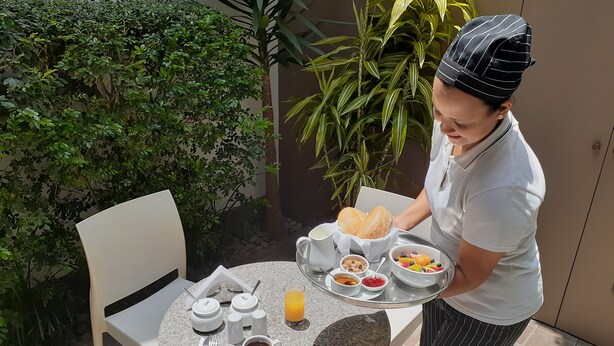 A person serving breakfast on a round table with a tray of food, including bread, fruit, and beverages. - Barranco Boutique Hotel by 3B  (Lima)