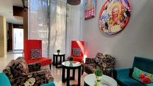 A modern living room with teal sofas, red chairs, and black tables. There are large windows with sheer curtains, a red pendant light, and artwork on the walls. - Barranco Boutique Hotel by 3B  (Lima)