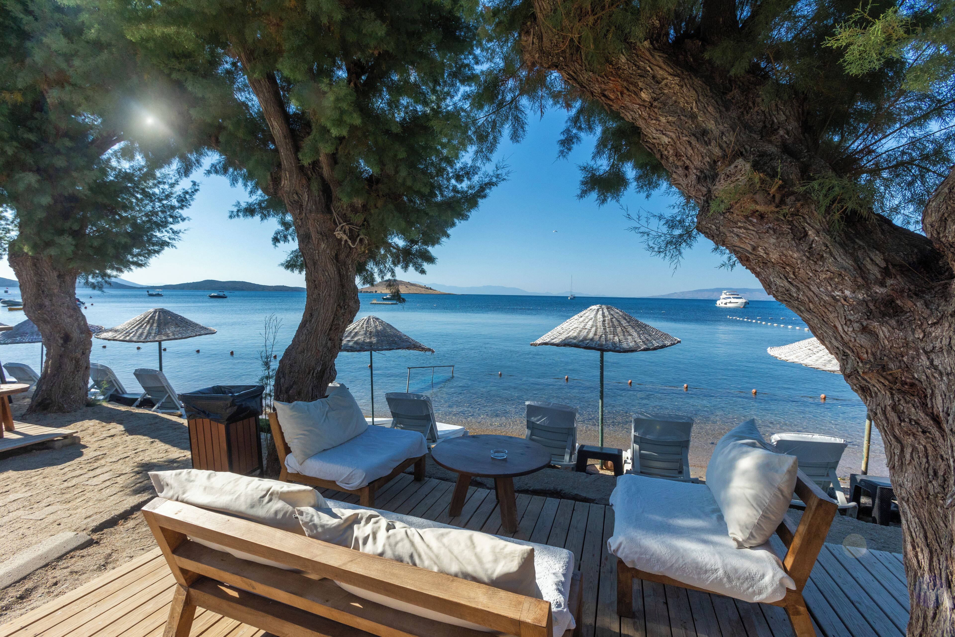A beachside lounge with wooden furniture, umbrellas, and a view of the sea.