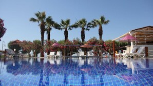 Una piscina con sillas de descanso y sombrillas, rodeada de palmeras y plantas con flores.