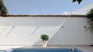 A pool area with a tiled floor, a white wall, and a potted plant. - Hotel Infanta Leonor (Ecija)