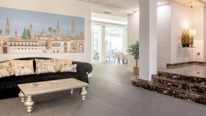 A modern hotel lobby with a black sofa, a marble coffee table, and a large cityscape painting on the wall. - Hotel Infanta Leonor (Ecija)