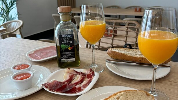 A breakfast setting with plates of food, glasses of orange juice, and a bottle of olive oil. - Hotel Infanta Leonor (Ecija)
