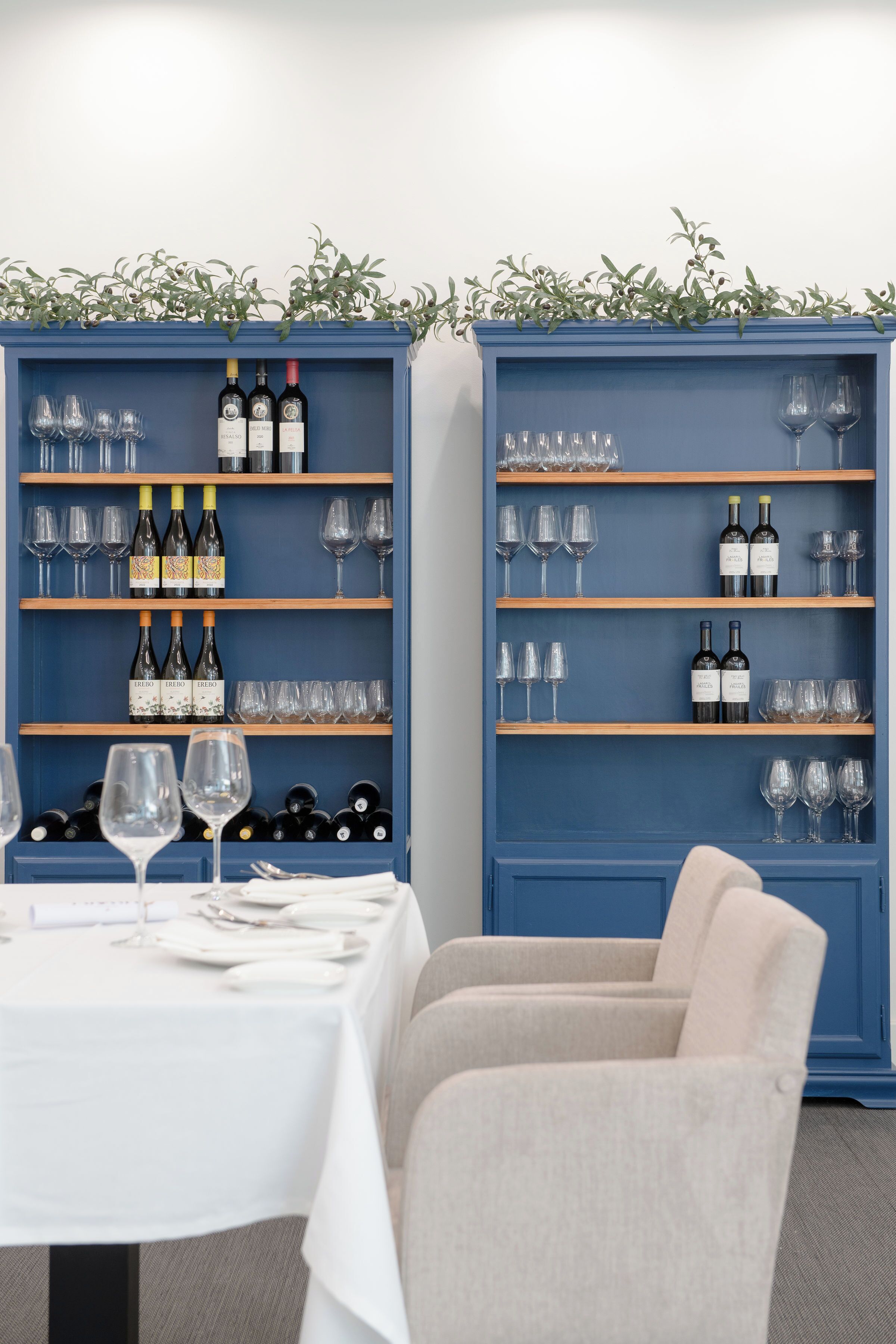A dining area with a table set for two, flanked by two blue wine shelves filled with bottles and glasses.