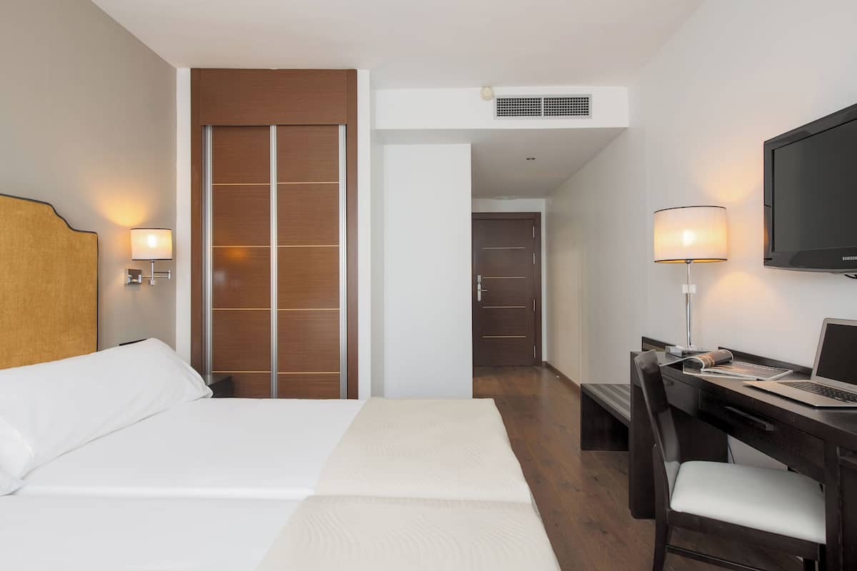 Habitación de hotel con cama, escritorio, silla, televisor y armario.