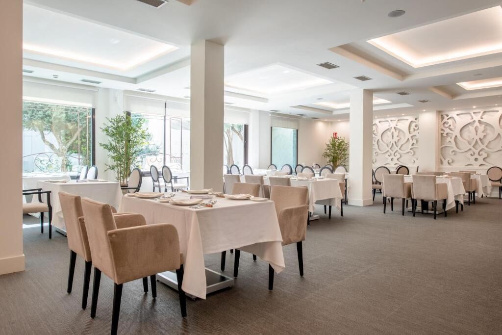 A spacious conference room with multiple tables and chairs, large windows, and decorative wall panels.