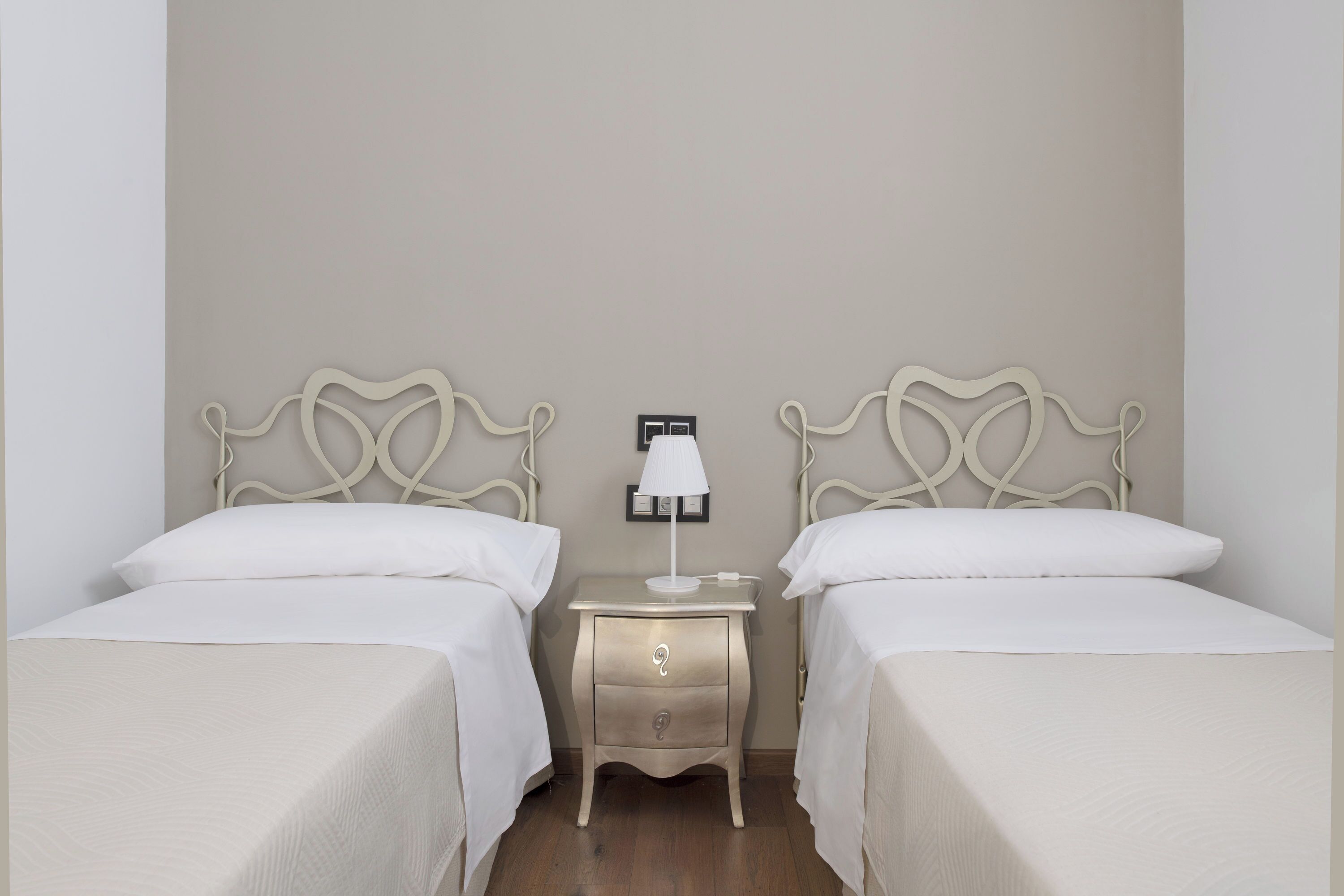 Un dormitorio con dos camas, una mesita de noche con lámpara y un cajón pequeño.