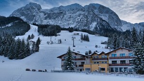 Une montagne enneigée avec un télésiège, un immeuble à plusieurs étages doté de balcons et une piste de ski.