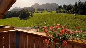 Une terrasse en bois offrant une vue sur un champ verdoyant, des montagnes et un télésiège.