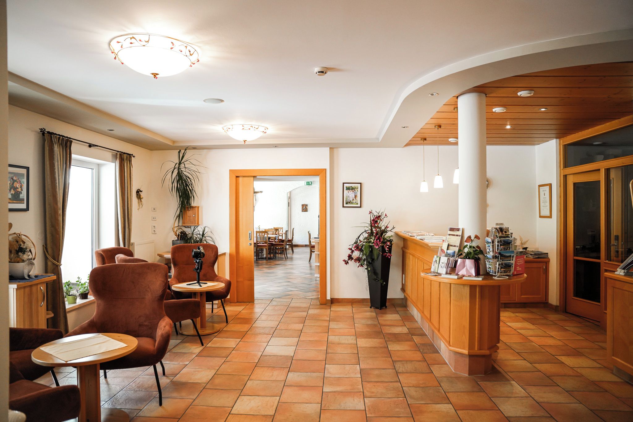 Eine Hotelhalle mit Empfangstresen, einer Sitzecke und einem Korridor, der zu einem Speisebereich führt.