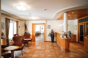 A hotel lobby with a reception desk, seating area, and a corridor leading to a dining area. - Gasthaus Landhotel Traunstein (Abtenau)