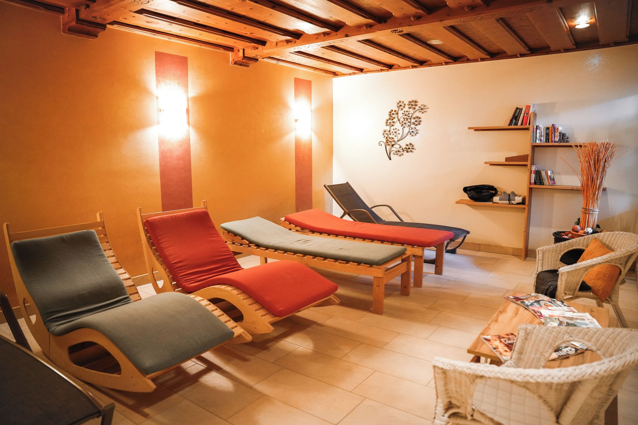 Una habitación luminosa con muebles de madera, incluyendo un sofá y sillas, y una estantería con libros y objetos decorativos.