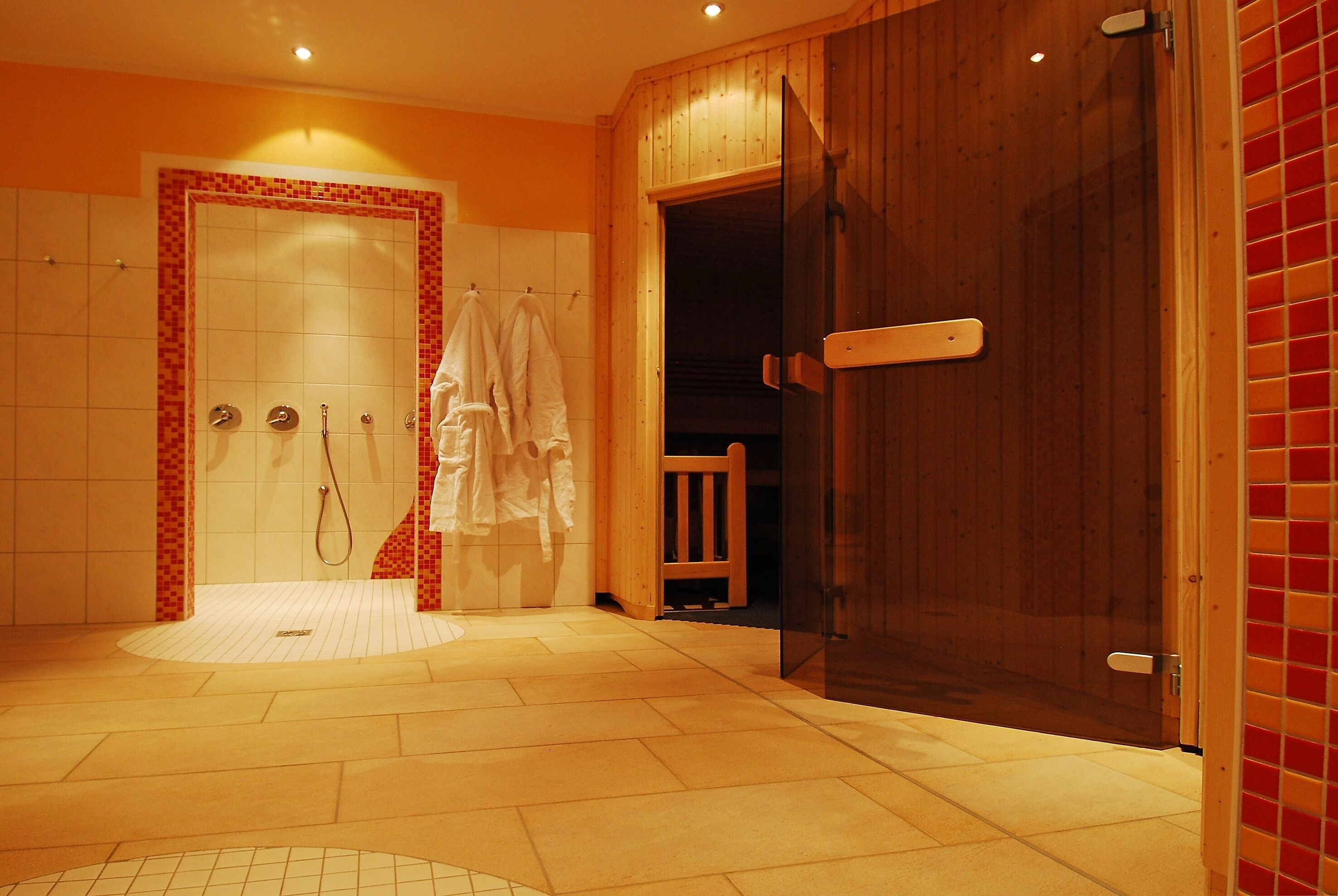 A modern bathroom with a shower, a wooden door, and a tiled floor.