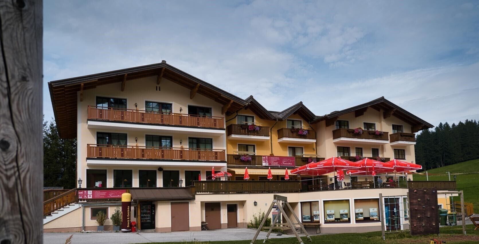 Un hôtel à plusieurs étages doté de balcons, d’un espace extérieur aménagé et surplombant une piste de ski.