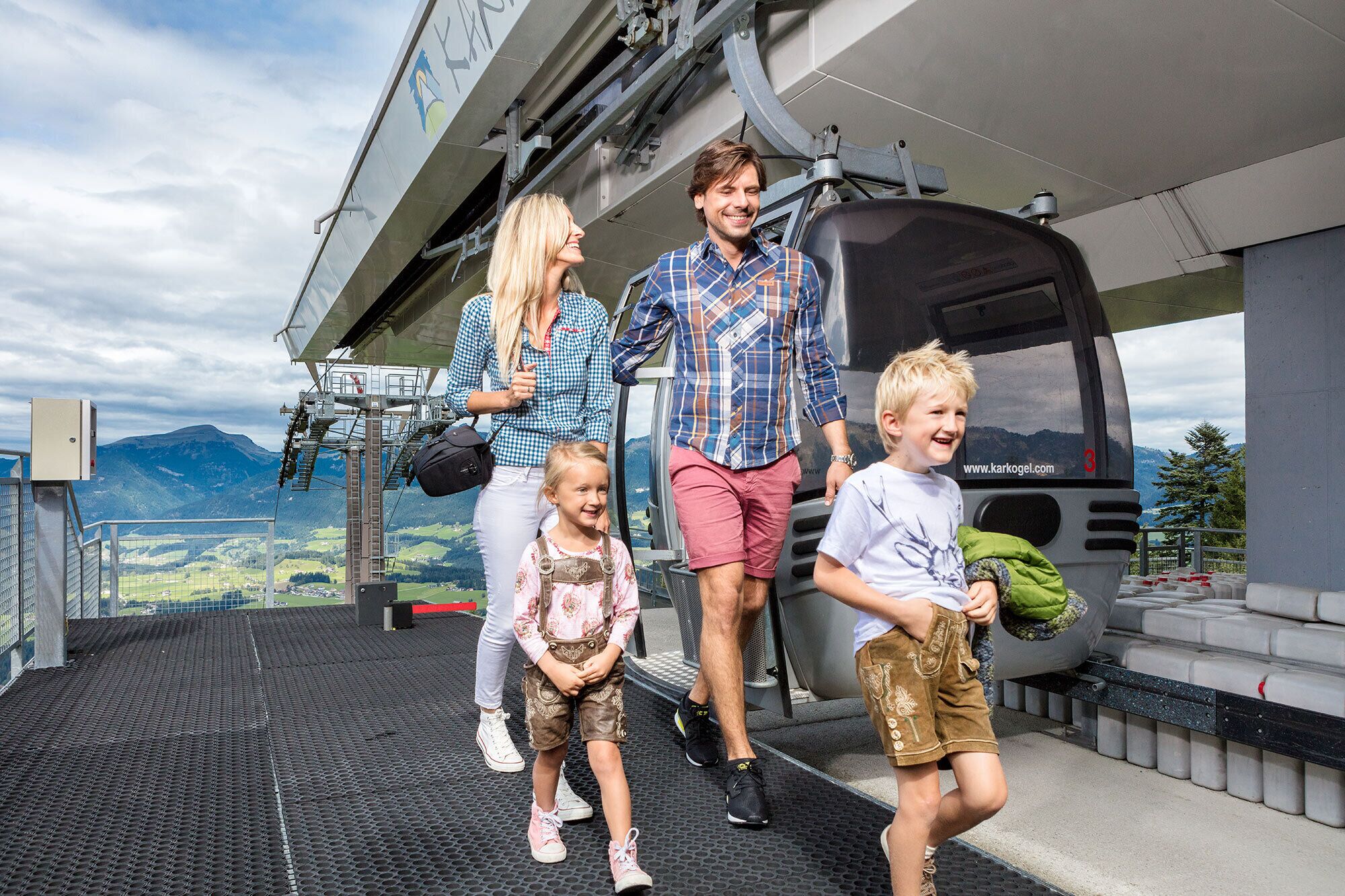 A family boarding a cable car with a scenic mountain view in the background.