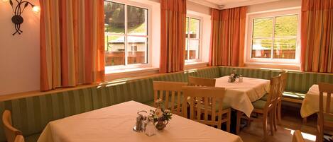 A dining area with tables and booths, large windows with curtains, and a wall-mounted light fixture.