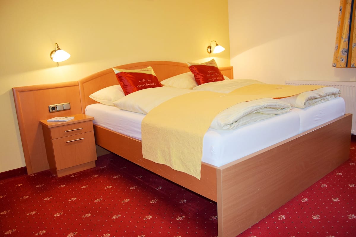 Un lit bien fait, avec une tête de lit en bois, deux tables de chevet avec des lampes et un sol recouvert d’une moquette rouge.