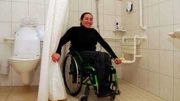 Un baño accesible para sillas de ruedas, con inodoro, ducha y barras de apoyo.