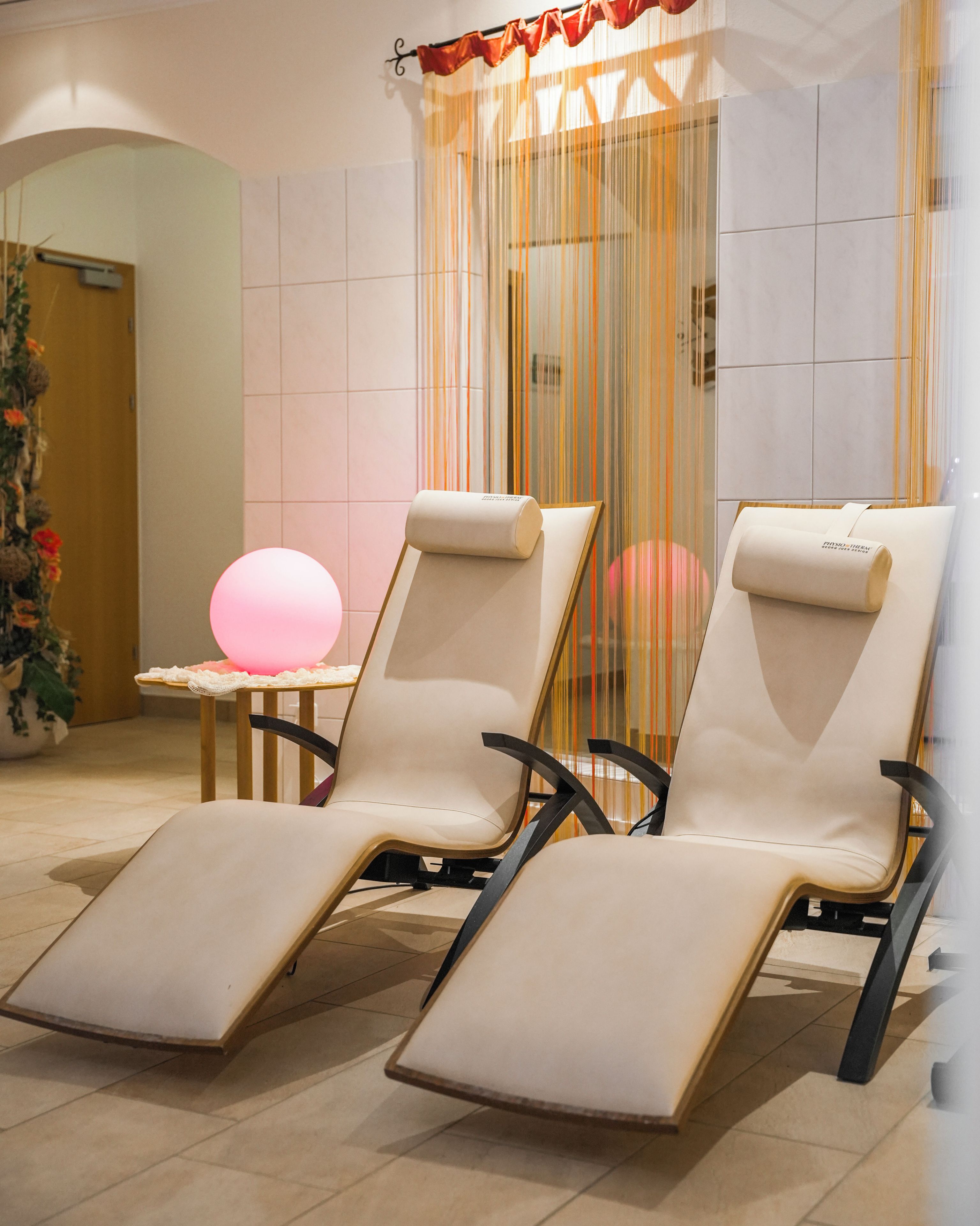 Un cuarto de spa con dos sillas reclinables, una mesa de masajes y una esfera rosa decorativa.