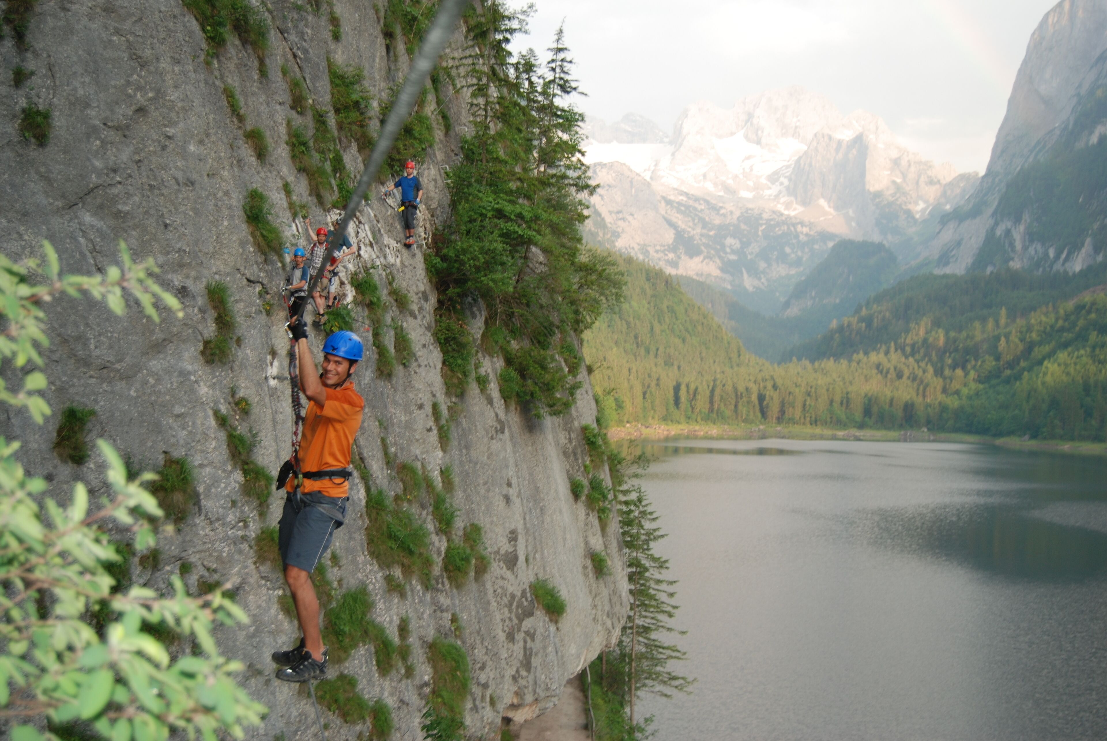 A person rappelling down a rocky cliff with a lake and mountains in the background.