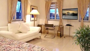 Una habitación de hotel con un sofá blanco, un escritorio, un televisor y una planta.