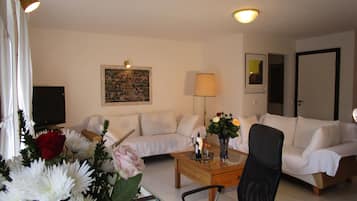 Un salon avec un canapé, une table basse, un téléviseur, un tableau et une lampe.