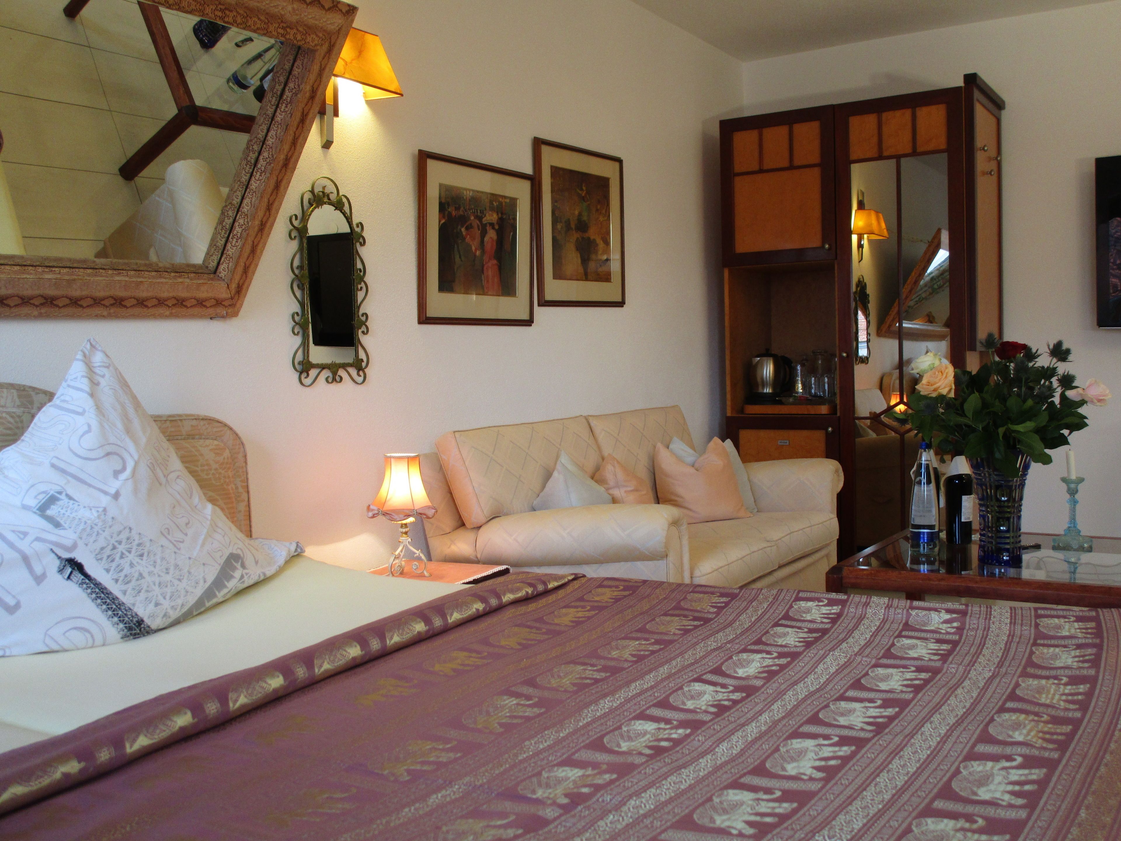 Habitación de hotel con cama, sofá, escritorio con lámpara, espejo y cuadros en la pared.