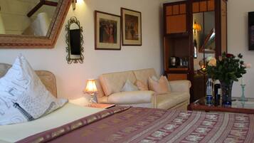 Habitación de hotel con cama, sofá, escritorio con lámpara, espejo y cuadros en la pared.