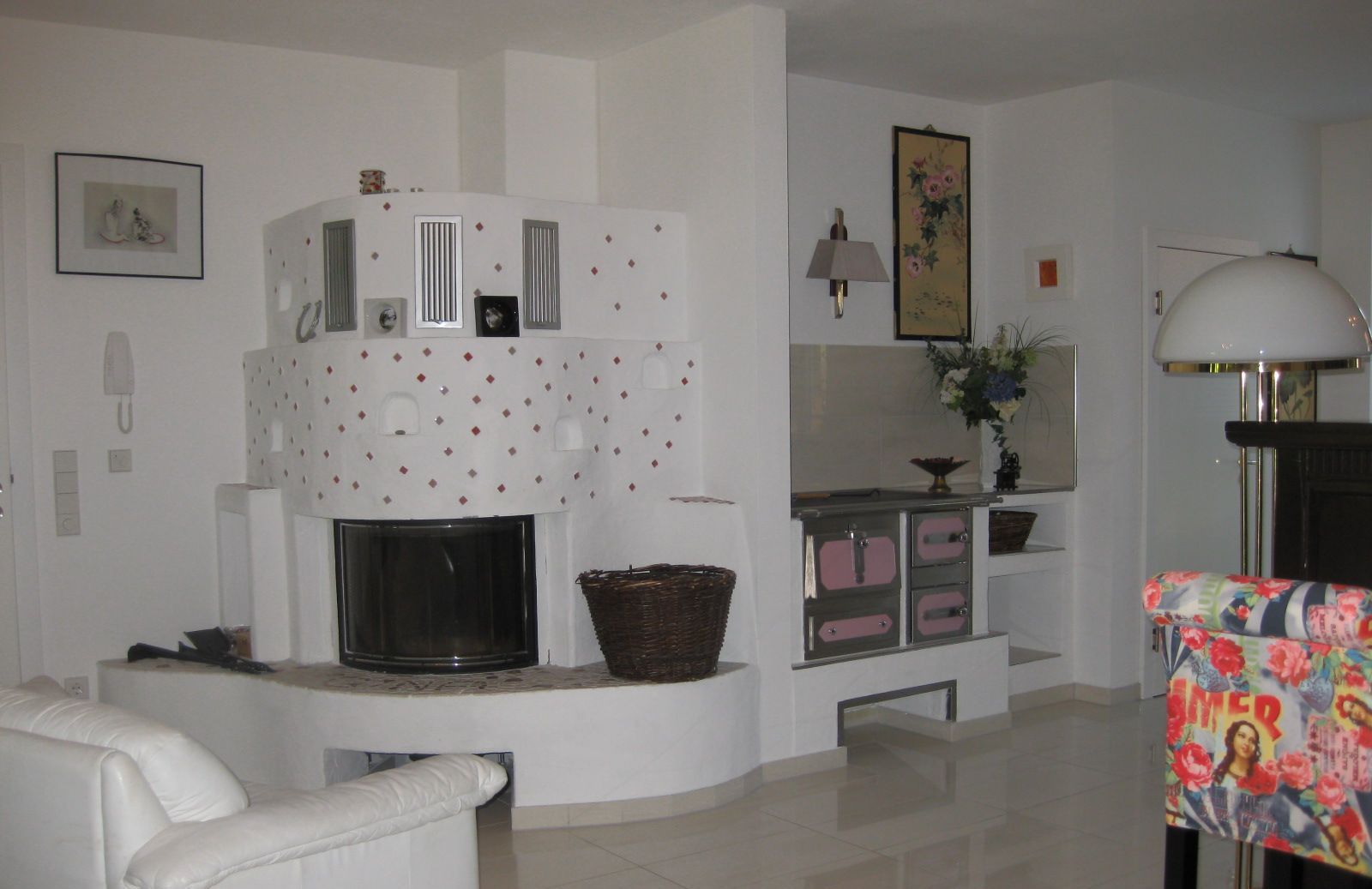A living room with a fireplace, white furniture, a kitchen area, and a colorful armchair.