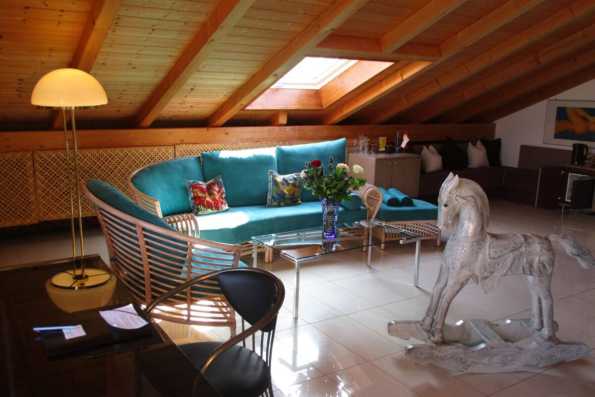 A cozy loft-style room with a curved teal sofa, a glass coffee table, and a metal sculpture of a horse.