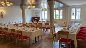 A dining area with multiple tables set for service, wooden chairs with red cushions, and chandeliers. - Le Saint Eloi (Solignac)