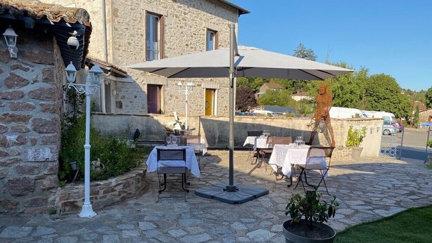 A stone building with outdoor seating, a potted plant, and a clear sky. - Le Saint Eloi (Solignac)