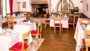 A restaurant with round tables, red cushioned chairs, a fireplace, and a stained glass window. - Le Saint Eloi (Solignac)