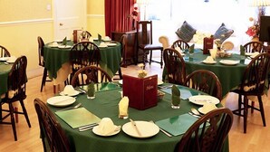 Un comedor con mesas redondas cubiertas de manteles verdes, sillas de madera y vajilla dispuesta con cuidado.