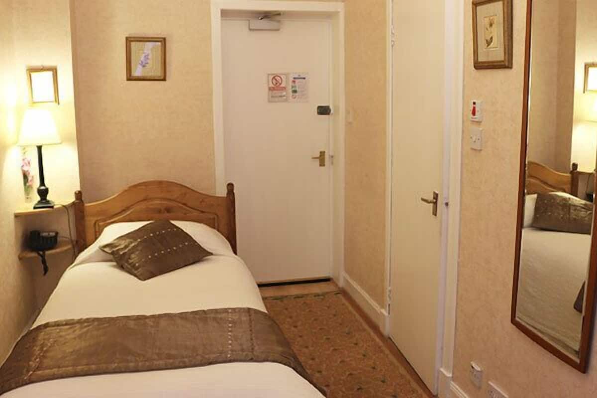 A hotel room with a bed, a bedside lamp, a door with a sign, and a mirror on the wall.