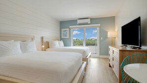 A hotel room with two beds, a TV, a desk with a chair, and a balcony with a view of greenery. - Fisher Inn Resort & Marina (Islamorada)