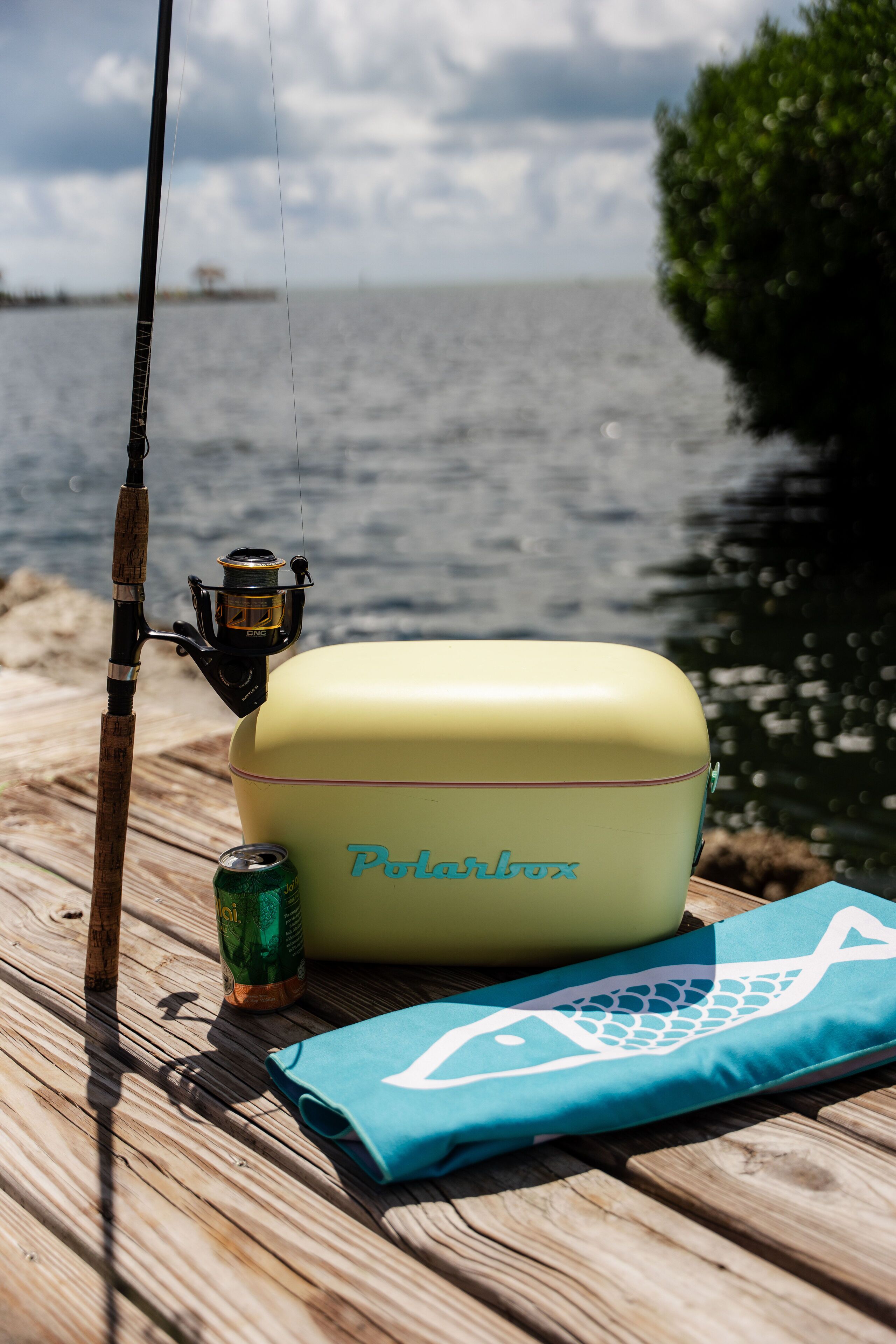 A fishing rod, a can of beer, and a yellow cooler with the brand name "Polarfox" on a wooden dock by a body of water.