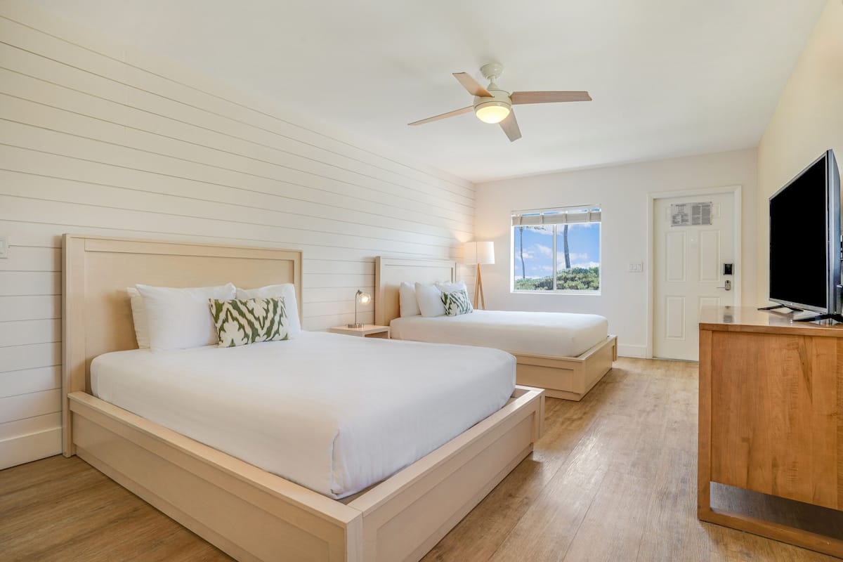 A bedroom with two beds, a ceiling fan, a TV, and a window with a view.
