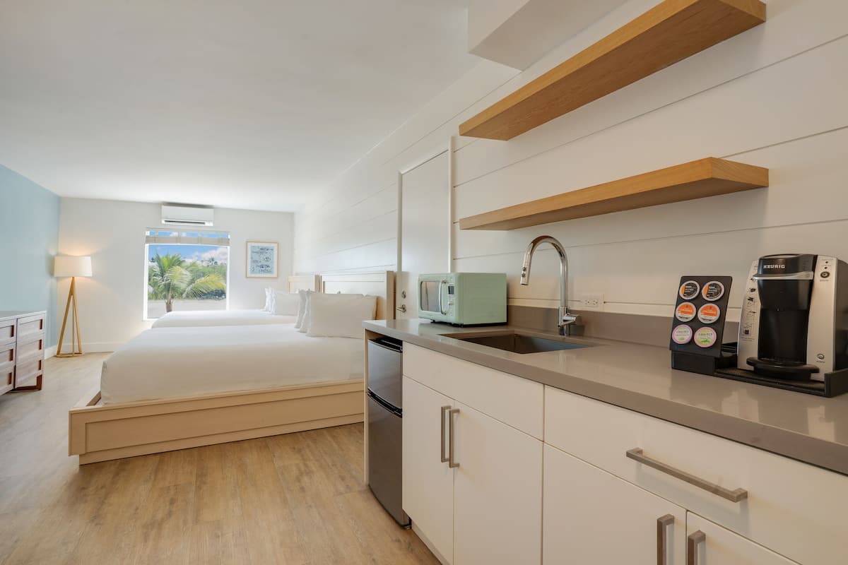A modern hotel room with a bed, kitchenette, and a view of palm trees.