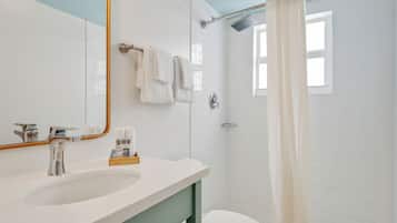 A bathroom with a white sink, a mirror, and a shower with a white curtain.