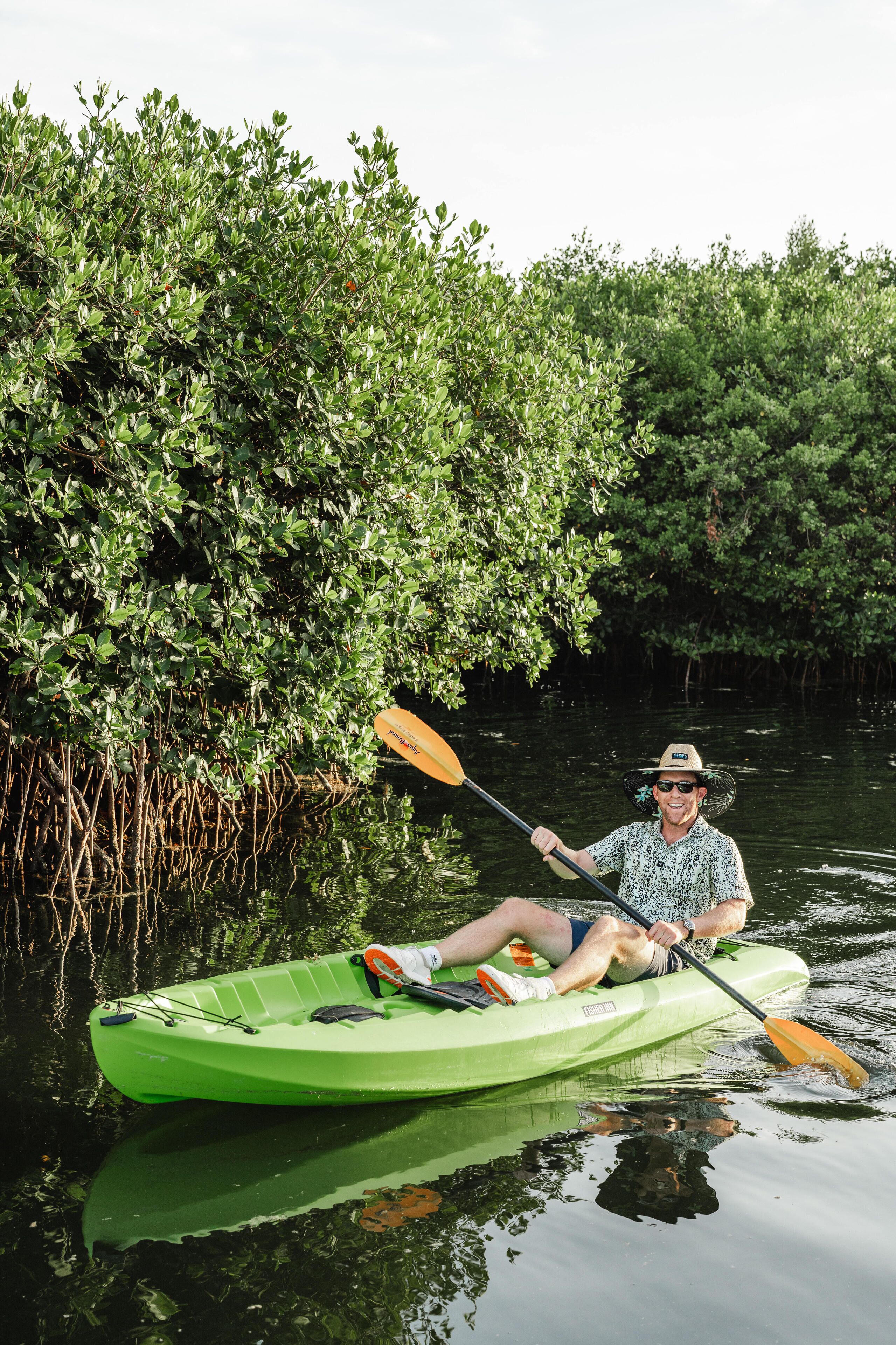 Una persona en un kayak verde sobre aguas tranquilas, rodeada de densa vegetación de mangle.