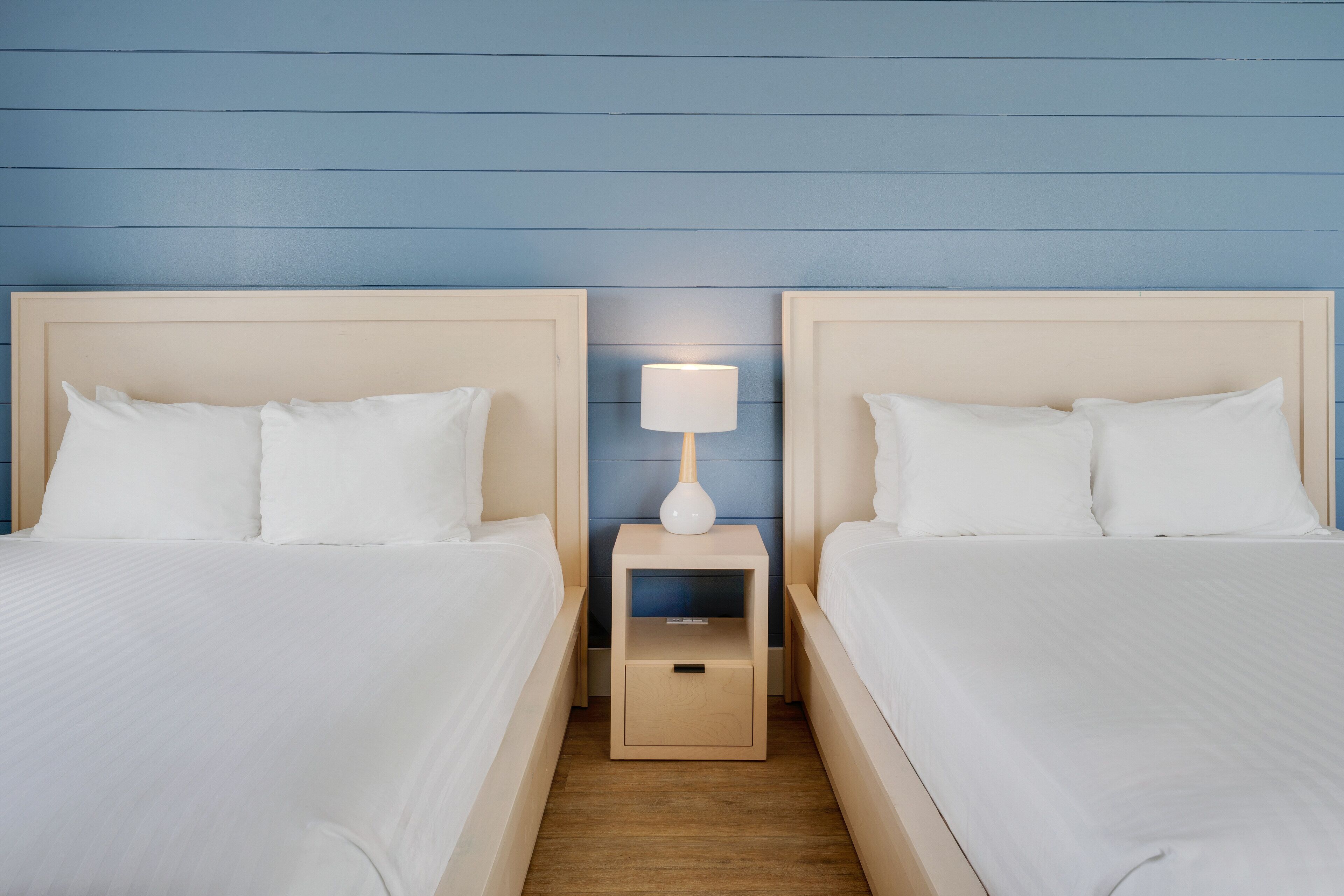 Ein Hotelzimmer mit zwei Betten, einem Nachttisch mit Lampe und Holzboden.