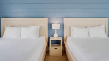 A hotel room with two beds, a nightstand with a lamp, and a wooden floor.