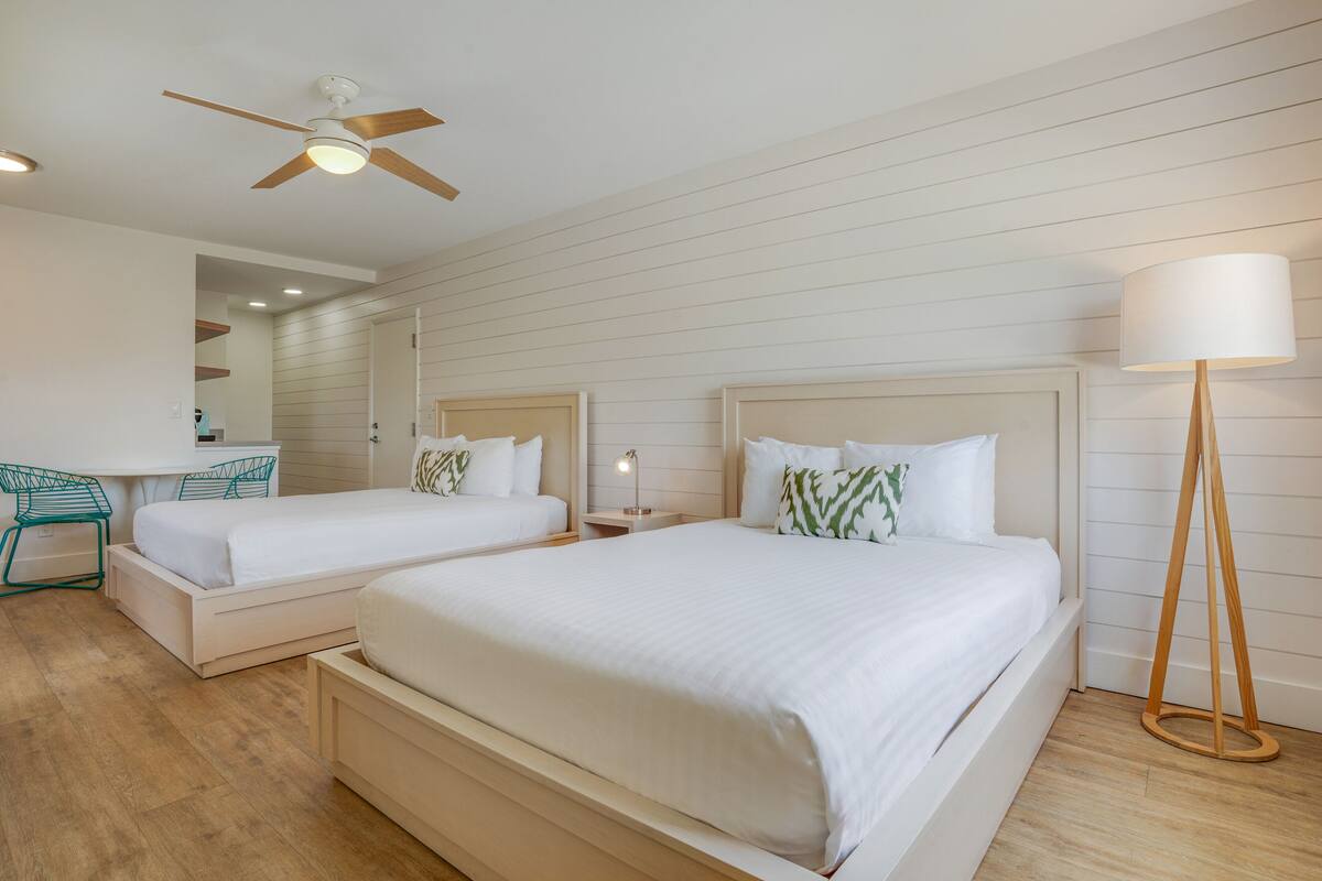 A hotel room with two beds, a desk, a chair, a ceiling fan, and a floor lamp.