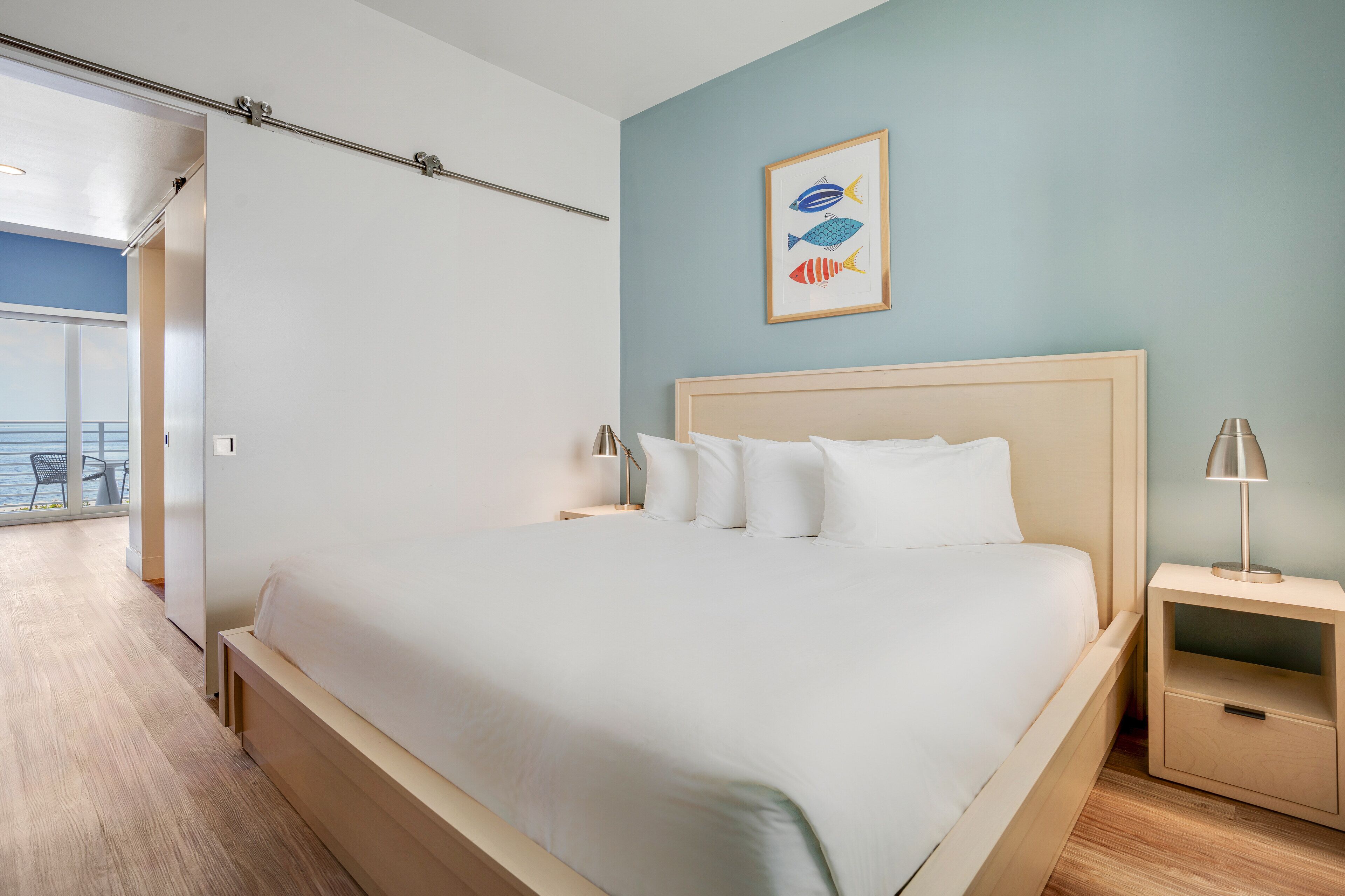A bedroom with a large bed, two bedside tables, a nightstand, and a wall-mounted picture of fish.